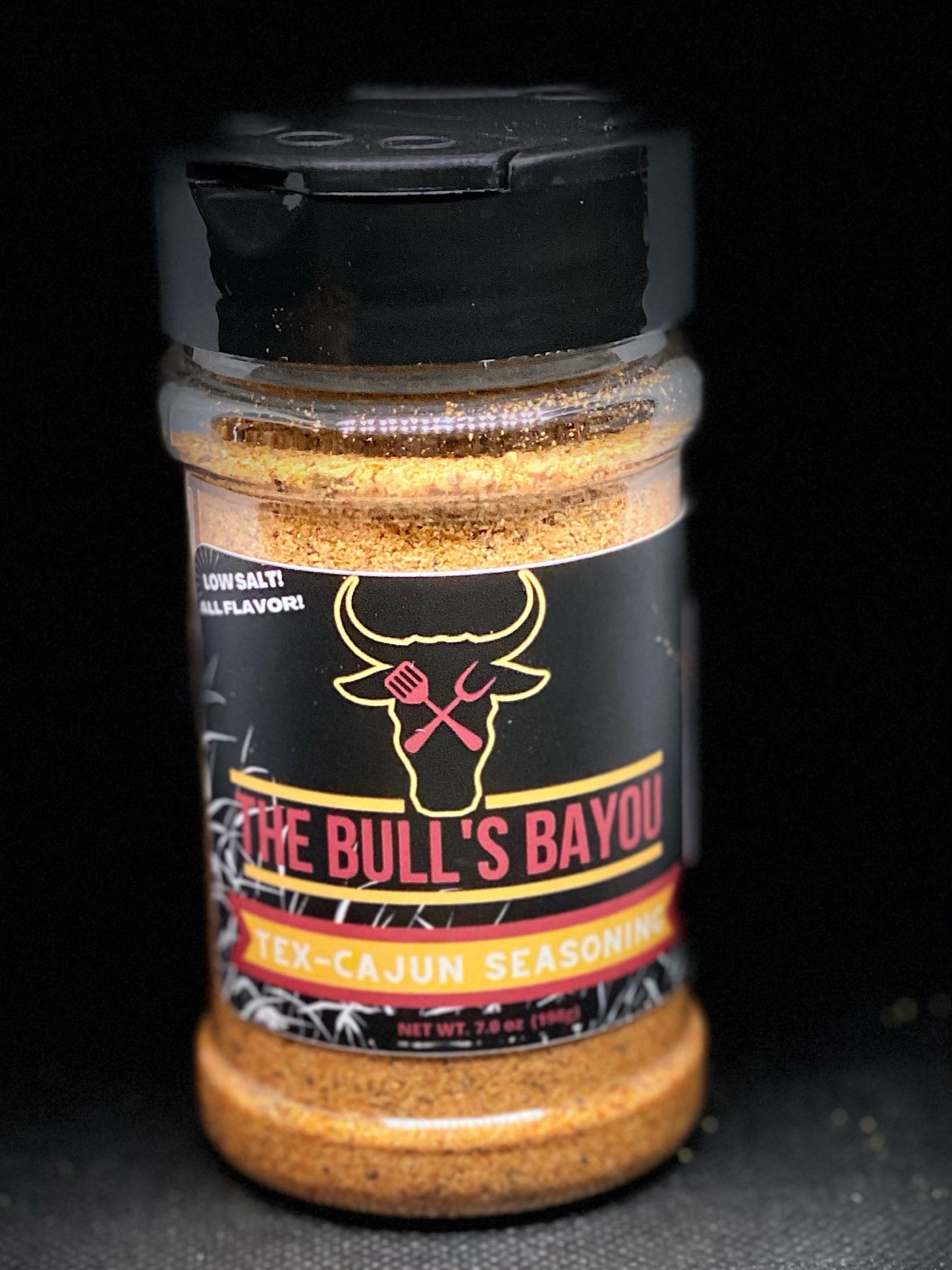 Image of a bottle of All Purpose Cajun Seasoning. The bottle has a black top with red text & a yellow outlined logo. The text on the bottle includes the product name, product description, ingredients, nutritional information, price, shipping information, social media links, and call to action.